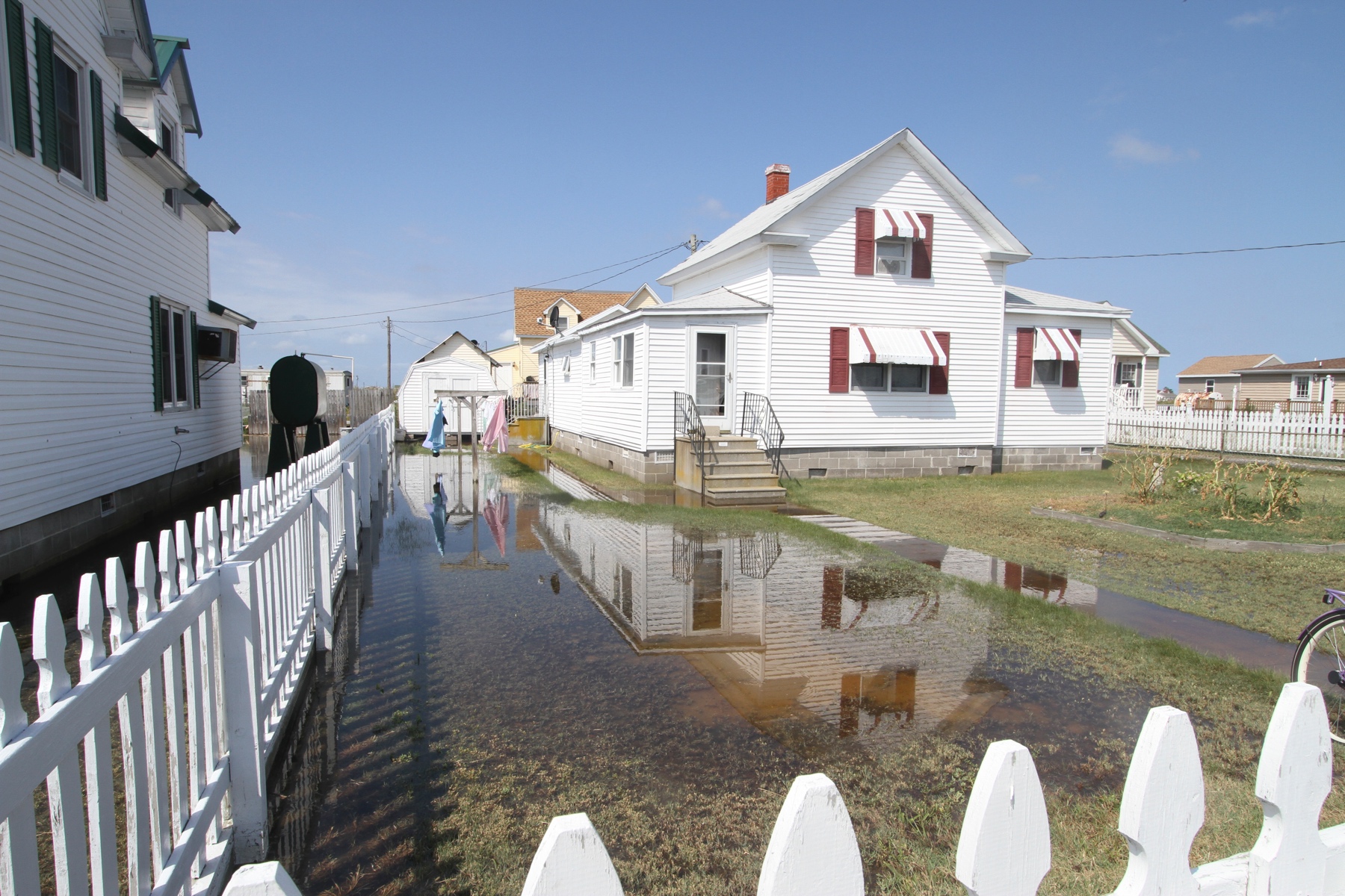 Town of Tangier occupied housing flooding at spring tide and recent precipitation. Note that the house has been raised, the walkway has not and is currently flooded. Most of the yard of the property has been converted to wetlands. Source: USACE, Norfolk District, Patrick Bloodgood, photographer.